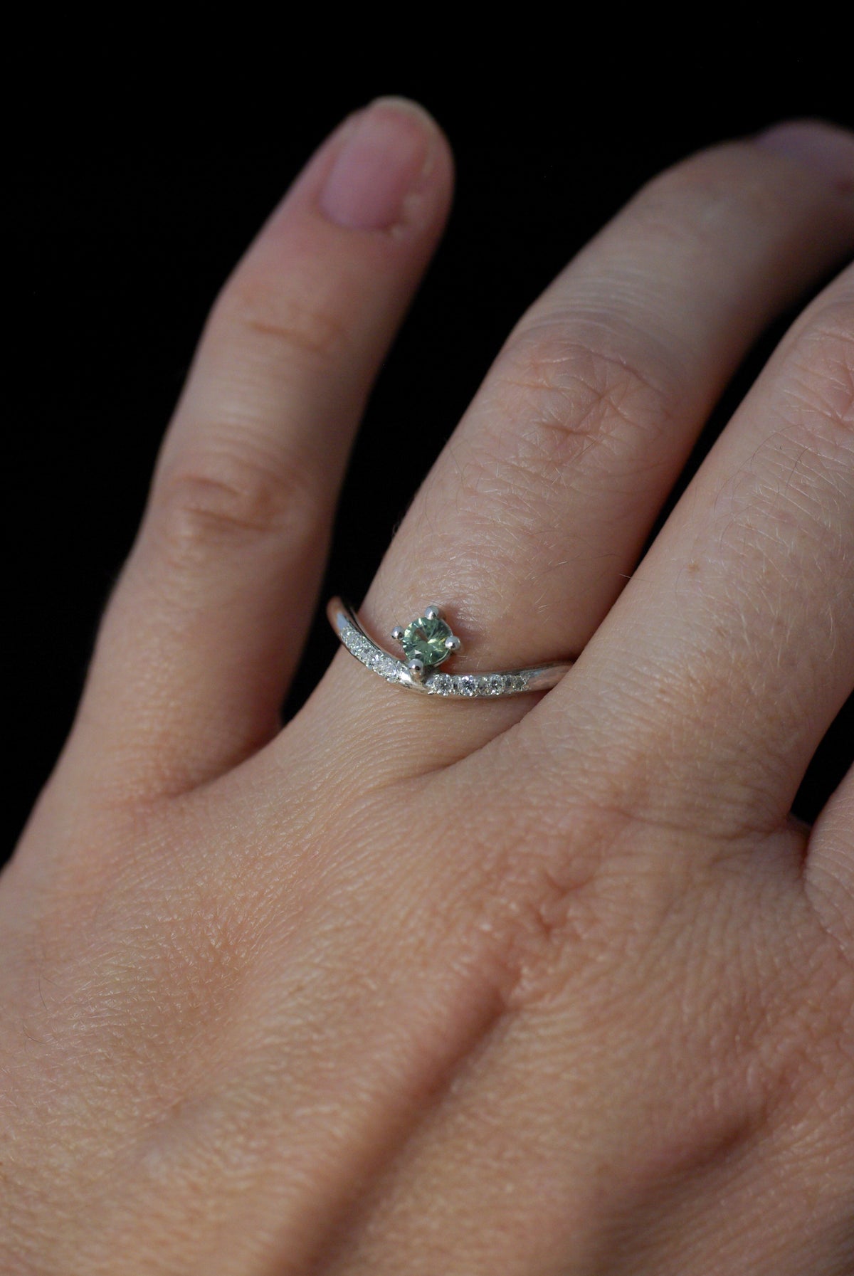 Vue sur le doigt d'une bague en argent, pierre verte et diamants sur un anneau ondulé