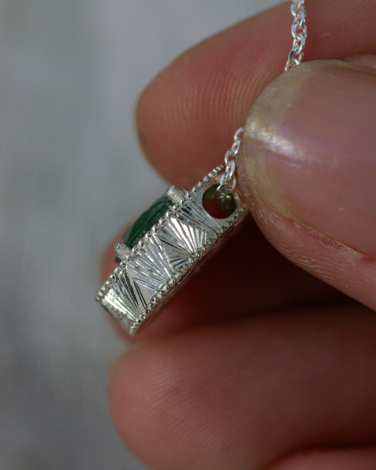 Côté d’un pendentif en argent entièrement gravé à la main avec chaînette traversant le bijou