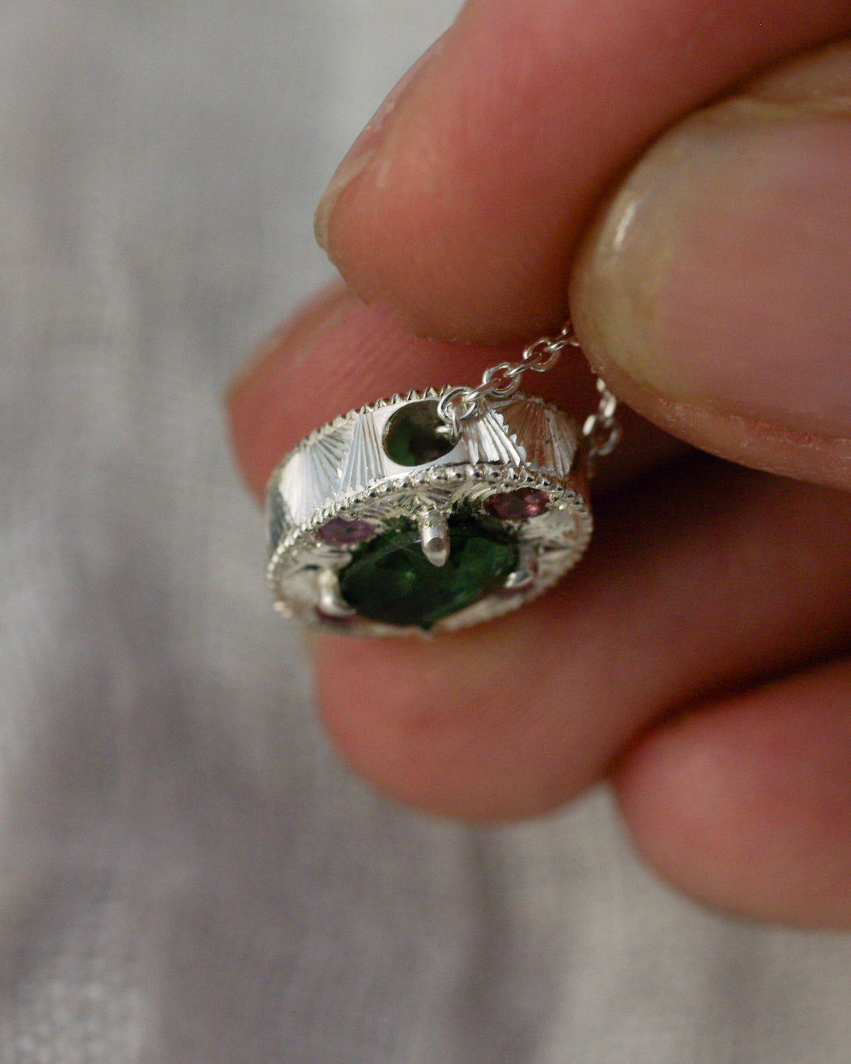 Détail de la chaîne traversant un pendentif en argent gravé à la main avec tourmalines et saphirs
