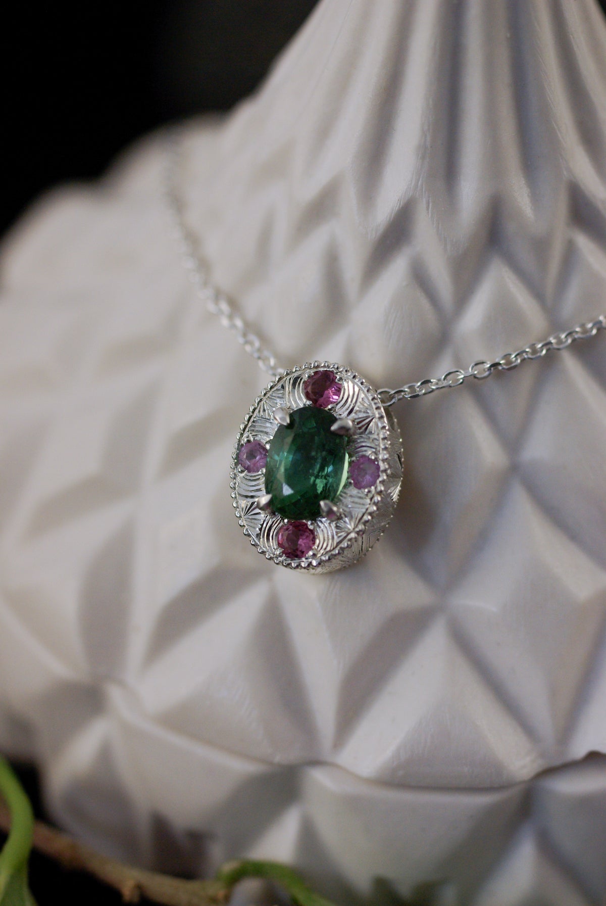 Mise en situation d'un pendentif artisanal en argent et tourmaline verte du Congo, gravure à la main et pierres roses aux quatre points cardinaux